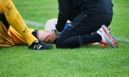 Sérült futballista fekszik a füvön, a csapatorvos gondosan ápolja