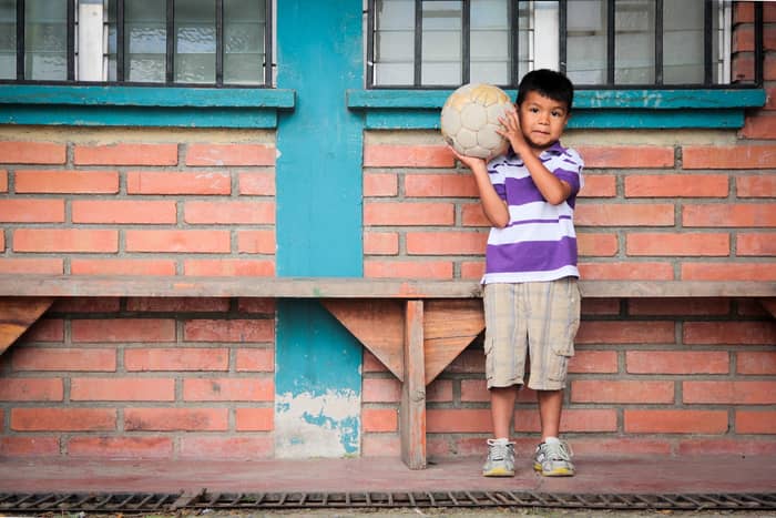 Kisfiú áll a falnál, focilabdával a kezében